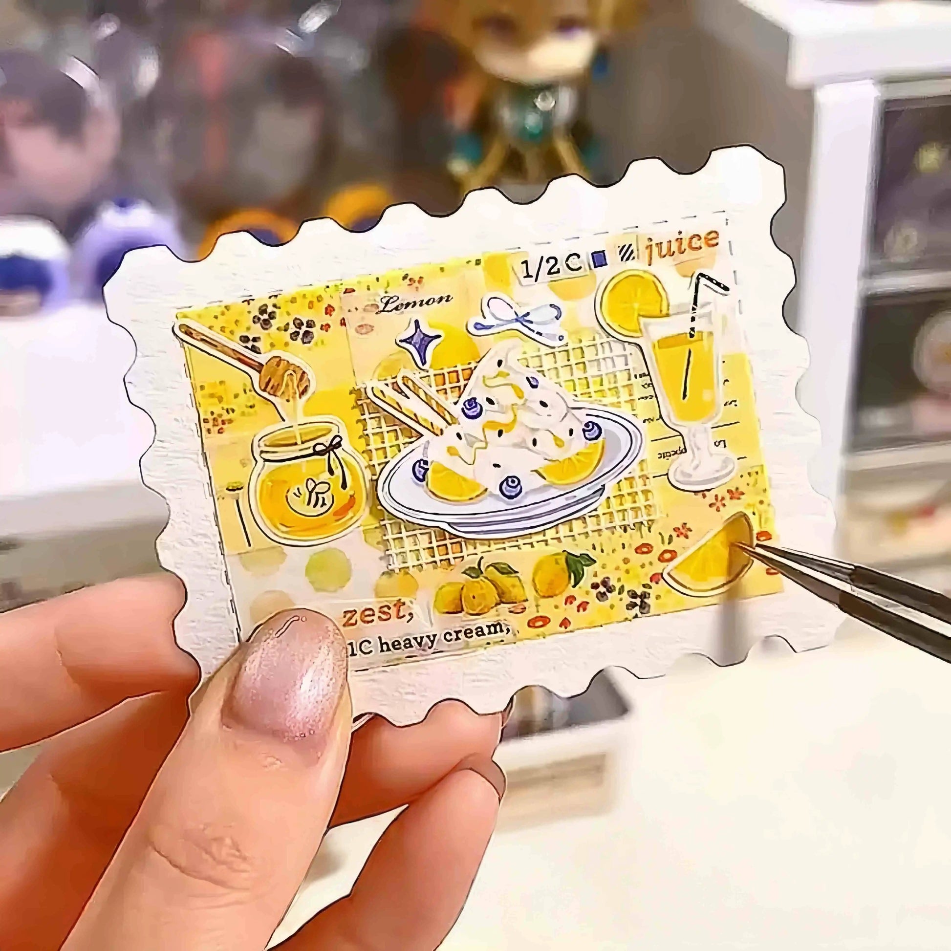 Completed journal insert with colorful food illustration painted on a blank stamp-shaped watercolor card, held with tweezers