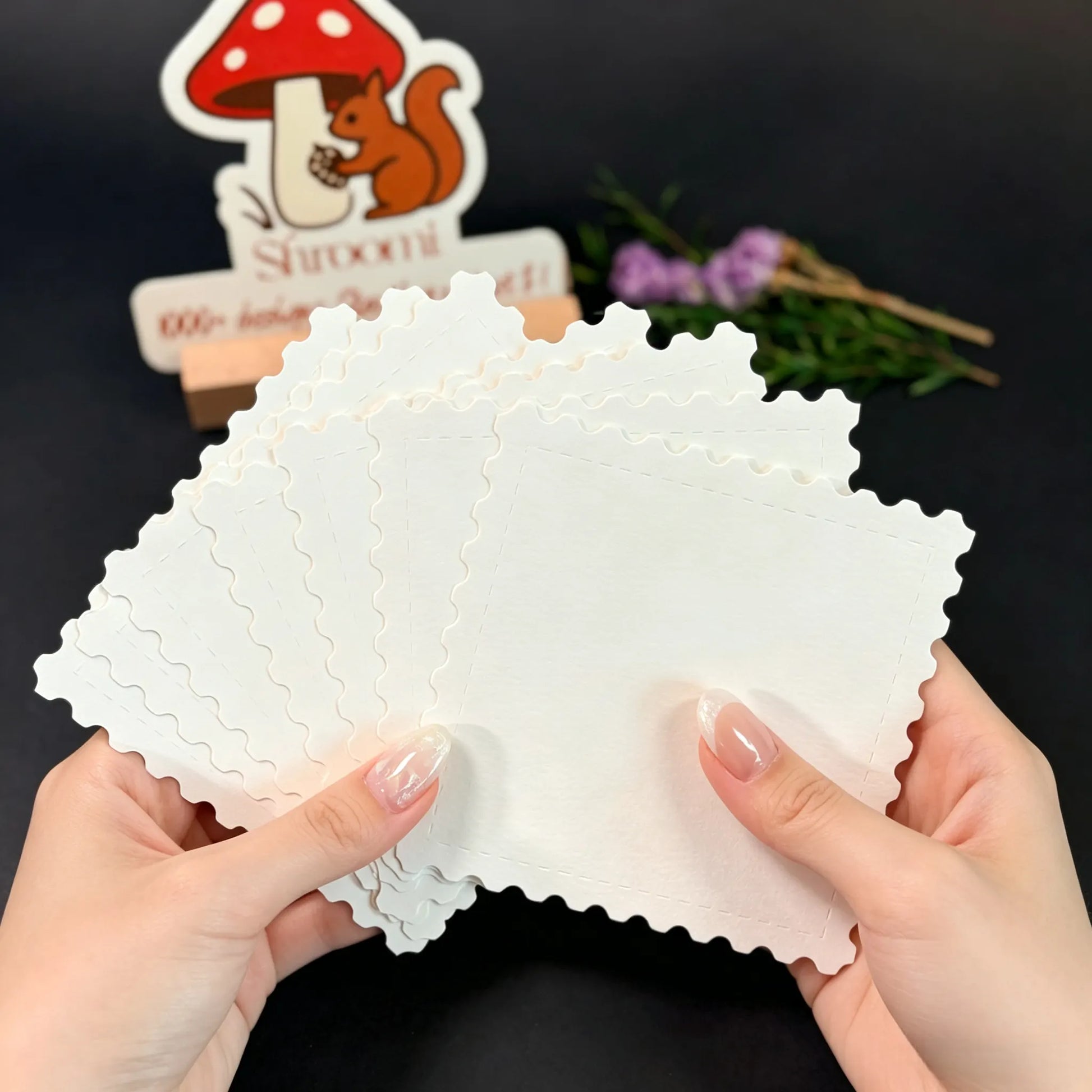 Fan of blank rectangular stamp-shaped watercolor paper cards with scalloped edges spread in two hands