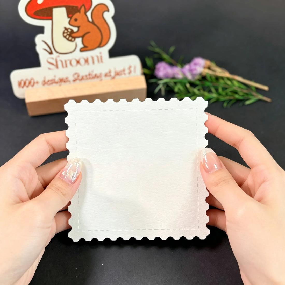 Hands holding a single 5.5x5.5cm blank square stamp-shaped watercolor paper card with scalloped edges