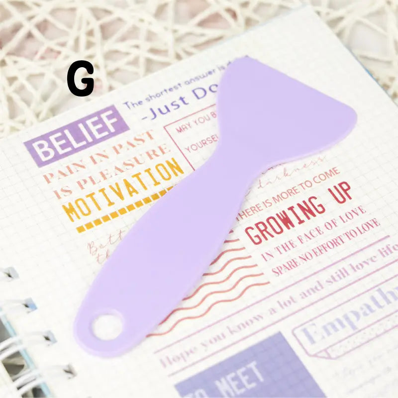 Handy plastic spatula in action, smoothing a vibrant sticker onto a surface with precision to ensure a flawless finish.