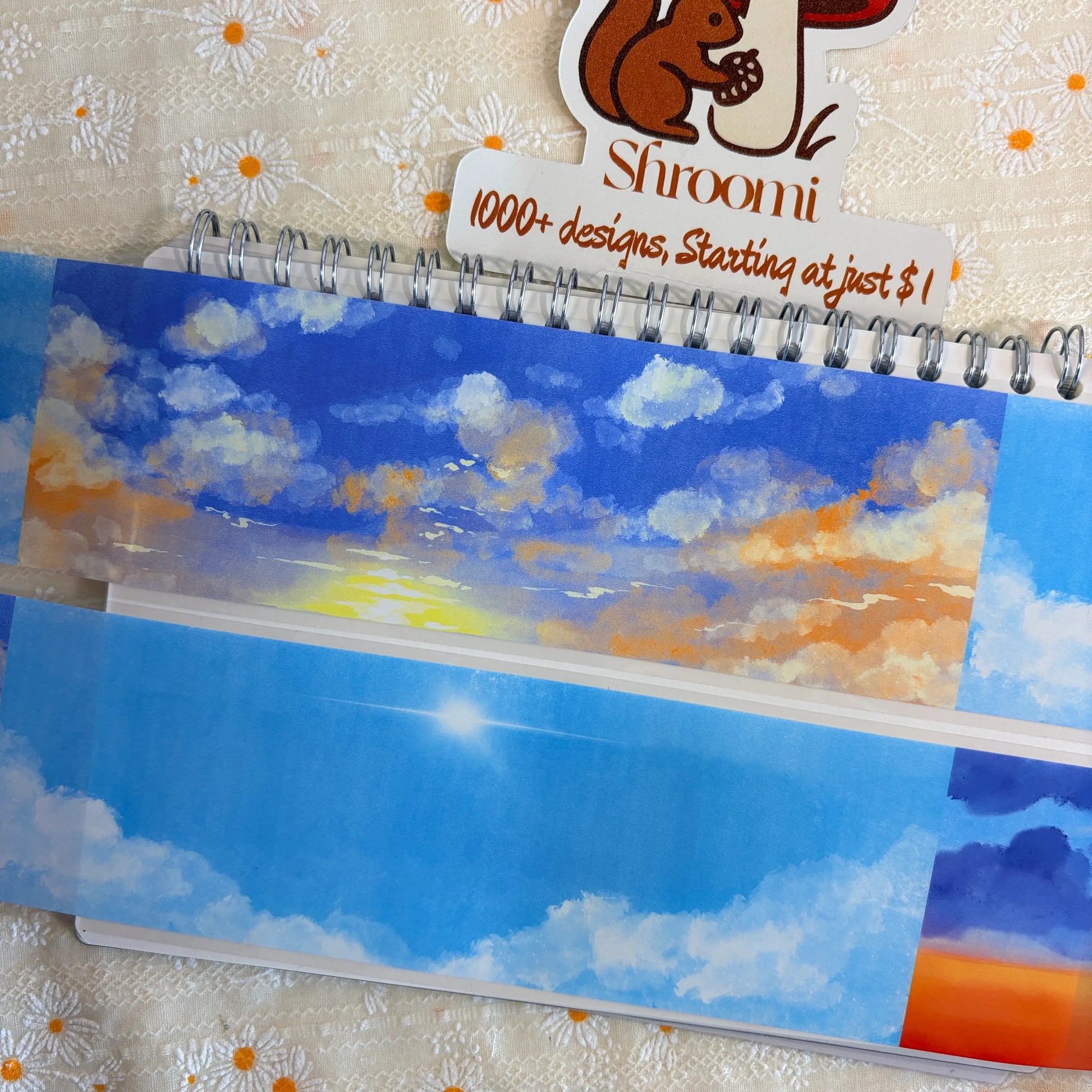 Shroomi Four Seasons Sky Background PET tape on journal — two strips: golden hour sky with glowing yellow sun and warm golden clouds (top), bright blue daytime sky with fluffy white cumulus clouds and radiant sun (bottom)