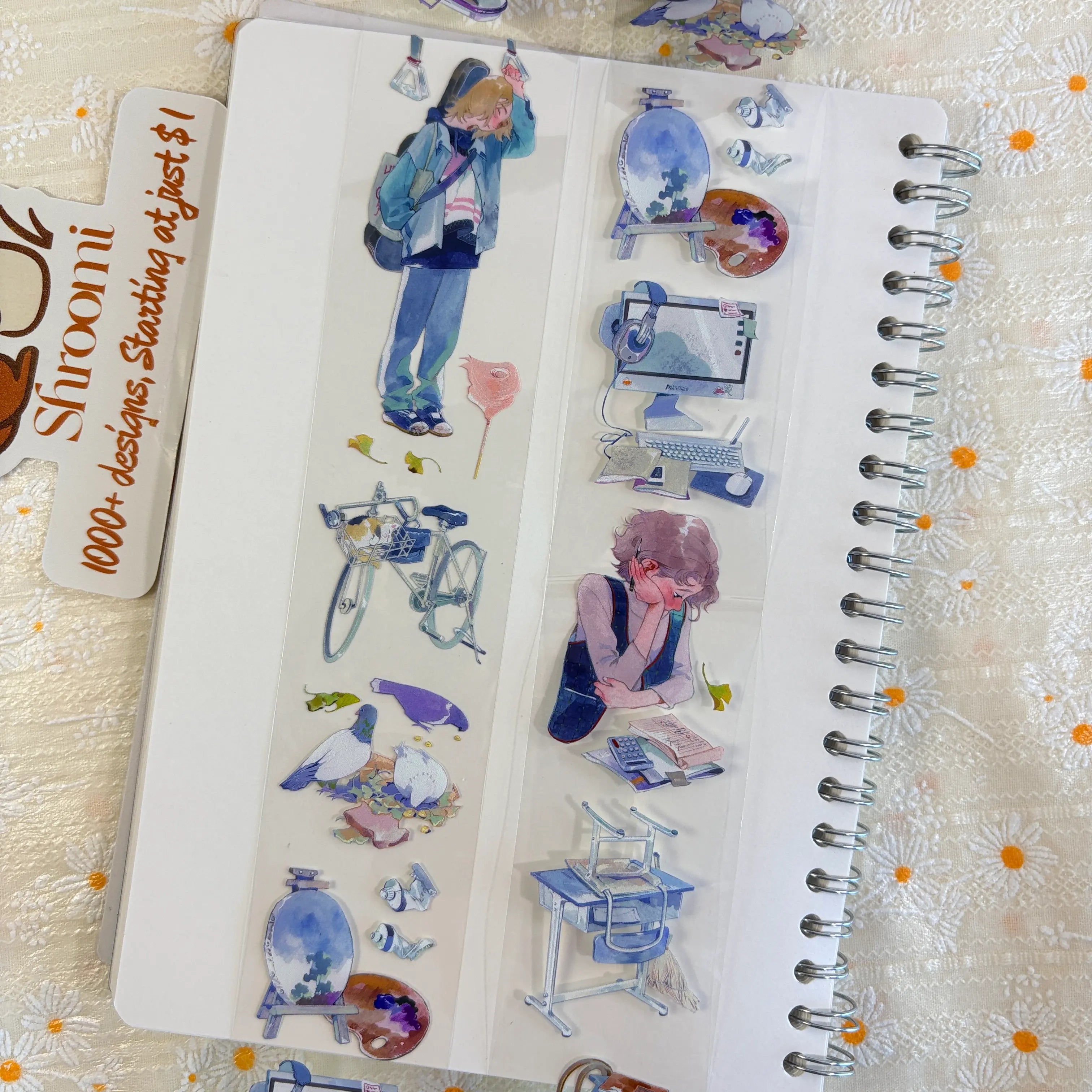 Shroomi PET tape on journal showing campus life: boy with blue jacket and backpack on phone, light blue bicycle, two white pigeons on coins, art easel with paint palette, computer desk setup, purple-haired student studying with calculator