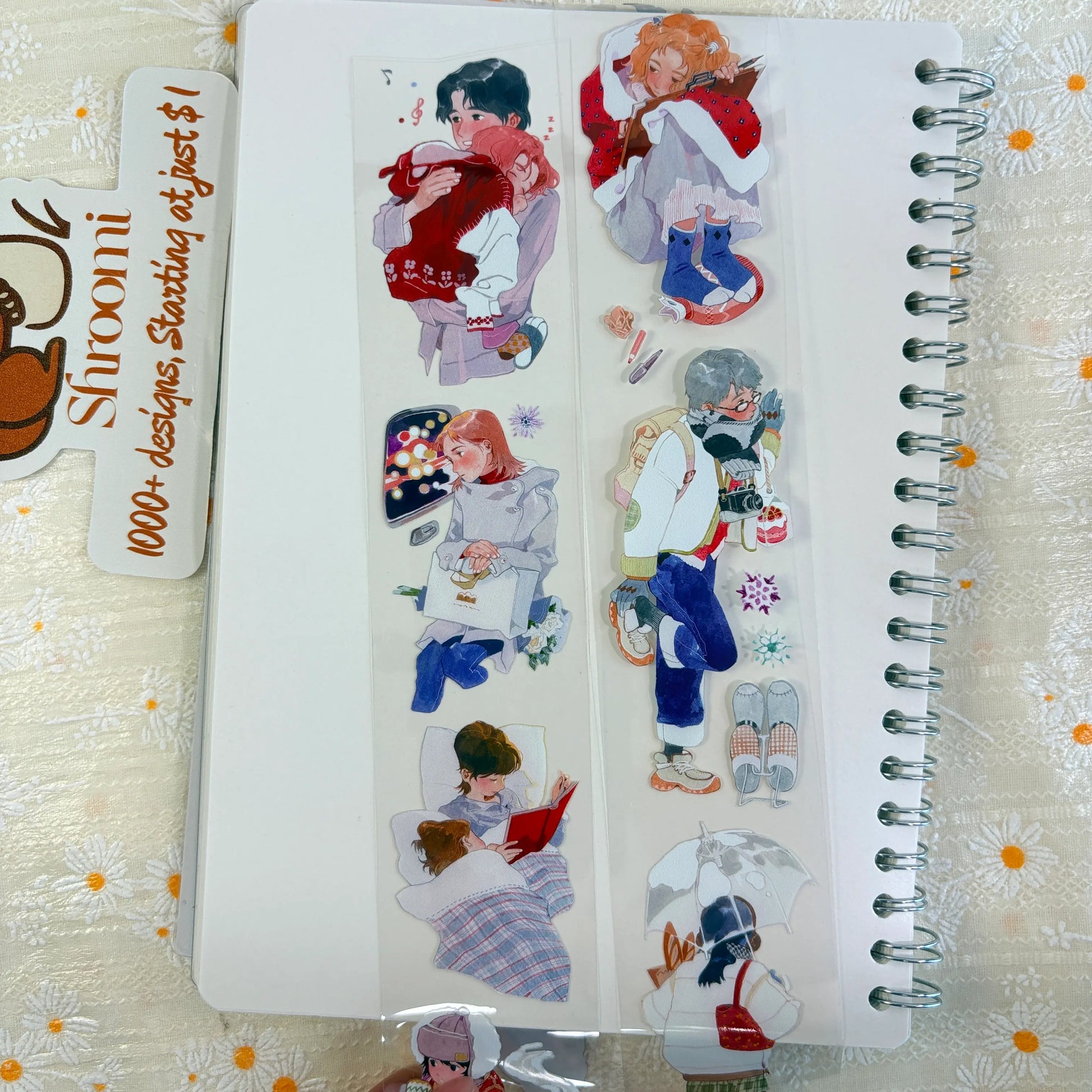 Shroomi PET tape on journal showing cozy winter moments: couple hugging, girl with string lights and shopping bags, man with camera and strawberry drink, couple reading in bed under plaid blanket