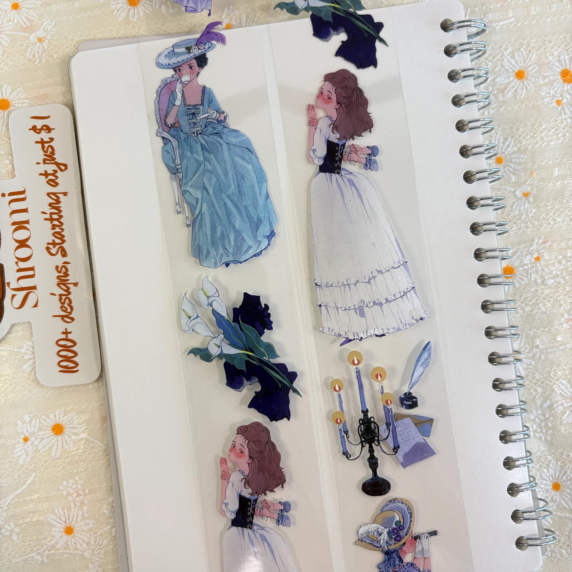 Shroomi PET tape on journal showing 18th-century ball scenes: woman in powder blue gown sipping tea, young woman in white ruffled gown, calla lilies, dark indigo irises, candelabra, blue feather quill with inkwell
