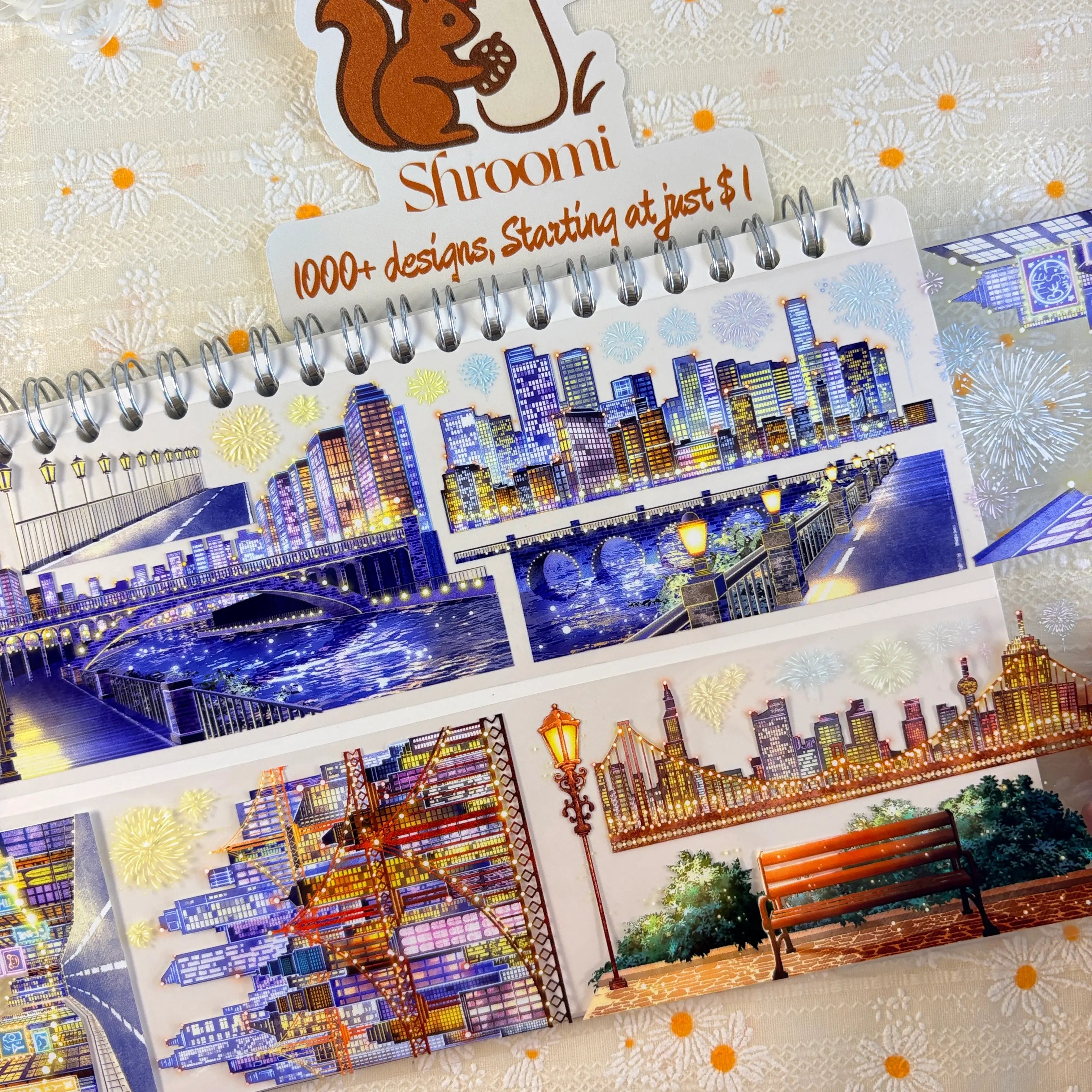 Shroomi Night City Shimmer PET tape on journal — two strips: night city with arched bridges over water and reflected skyscrapers (top); city skyline with park bench, lamp post, trees, and fireworks (bottom)