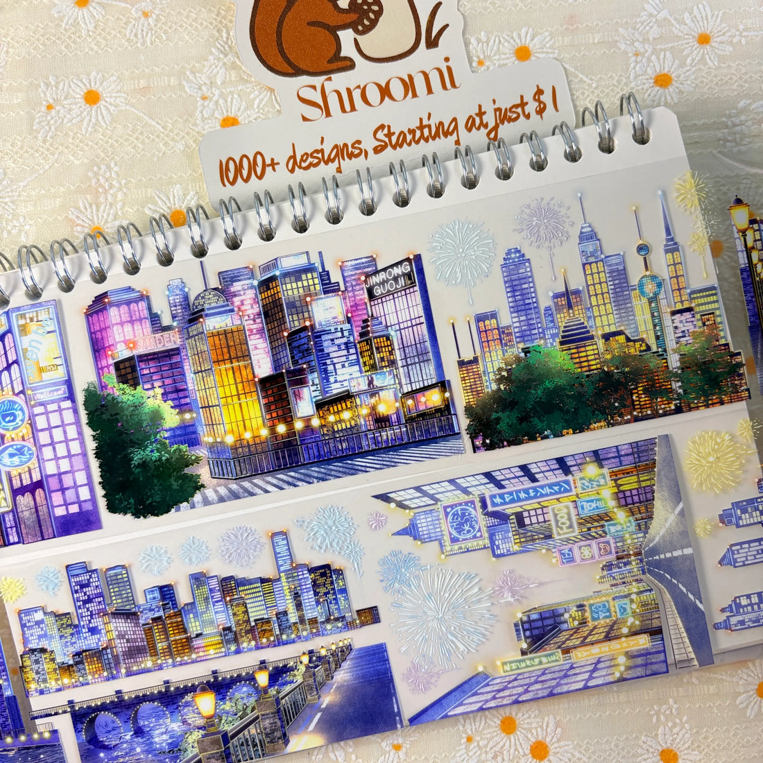 Shroomi Night City Shimmer PET tape on journal — two strips: blue-purple night skyline with illuminated skyscrapers and fireworks (top); city skyline with communications tower, fireworks, and lamp-lit bridge over water (bottom)