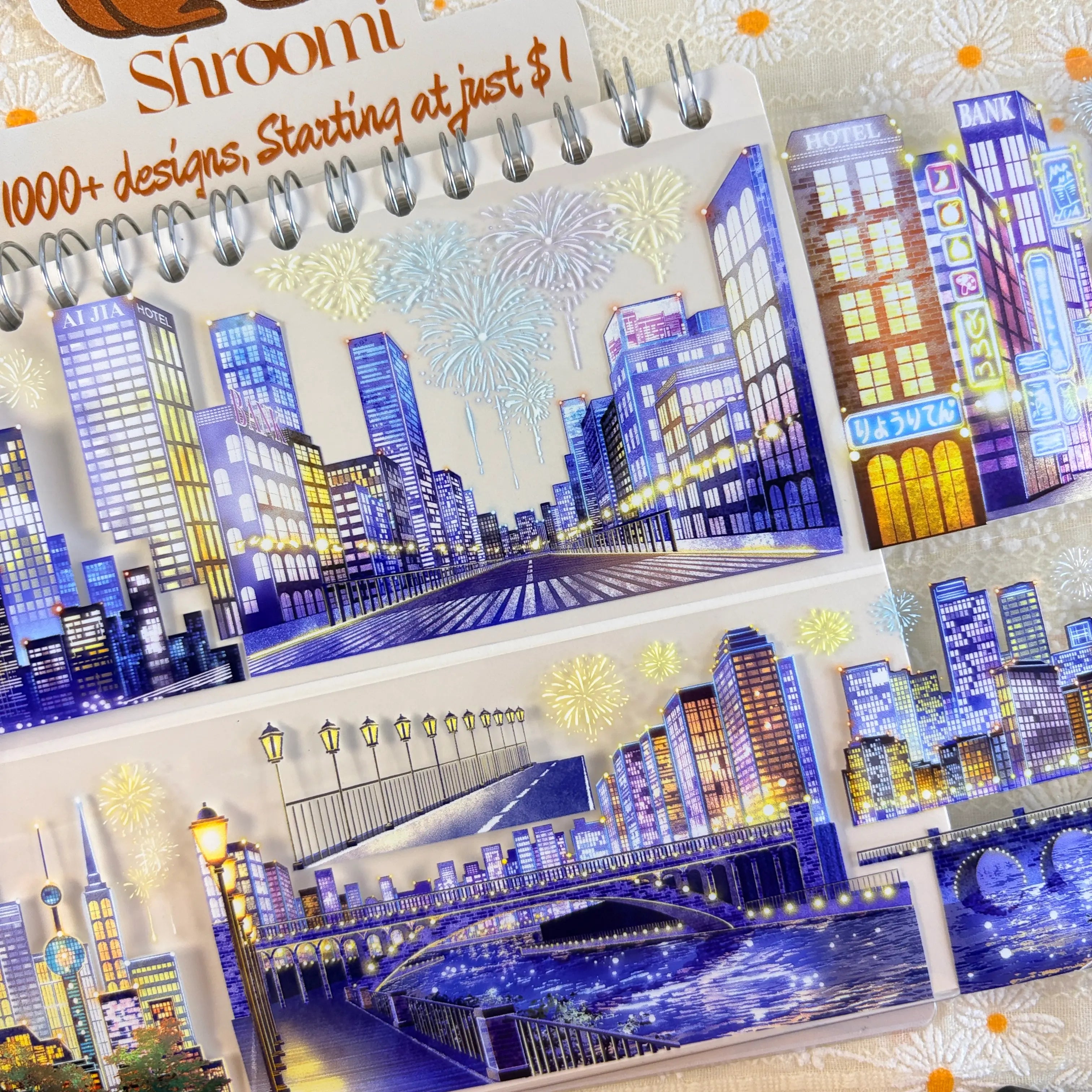 Shroomi Night City Shimmer PET tape on journal close-up — two strips: urban road with lit skyscrapers and fireworks (top); arched bridge with lamp posts and waterfront night cityscape (bottom)