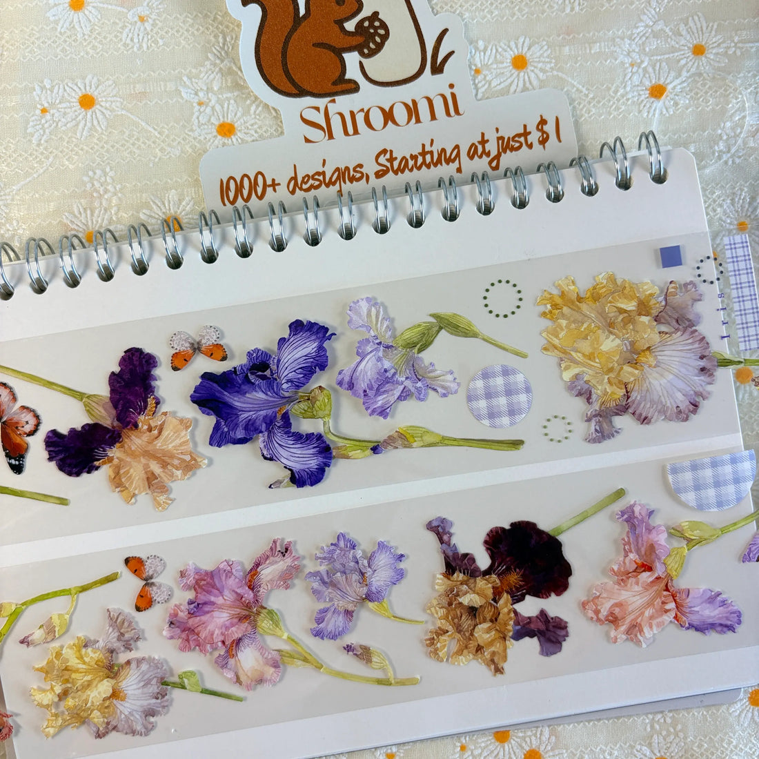 Two strips of Iris Blooms PET tape on a spiral notebook showing botanical iris flowers in purple, gold and cream with butterfly accents