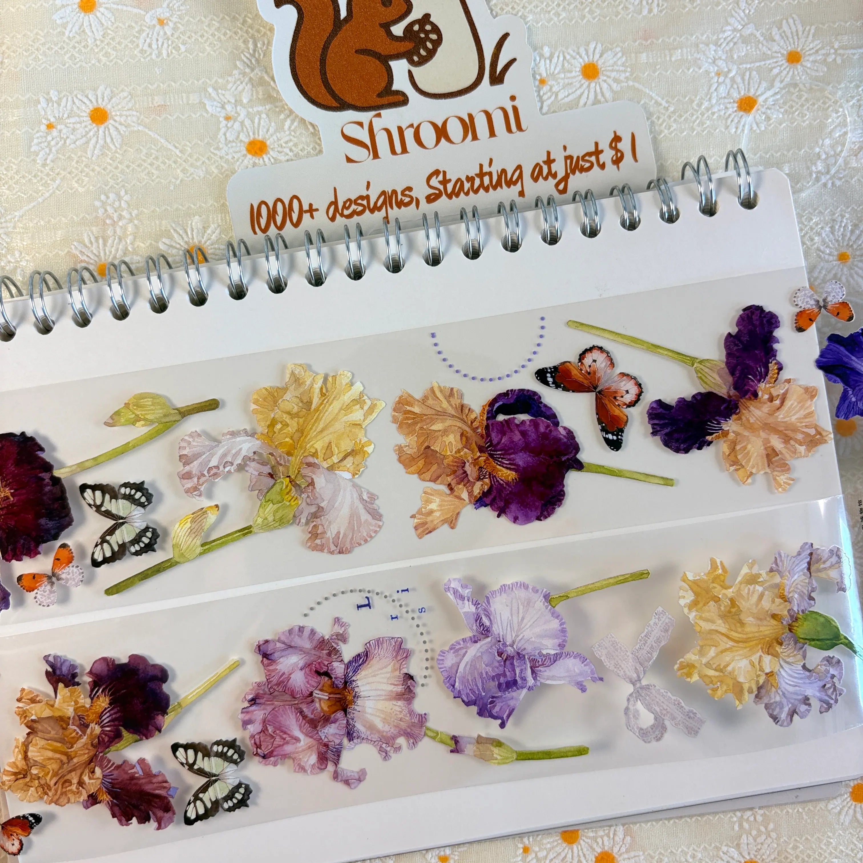 Two strips of Iris Blooms PET tape on a spiral notebook showing botanical iris flowers in purple, gold and cream with butterfly accents