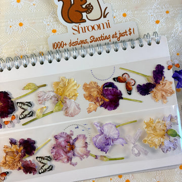 Two strips of Iris Blooms PET tape on a spiral notebook showing botanical iris flowers in purple, gold and cream with butterfly accents