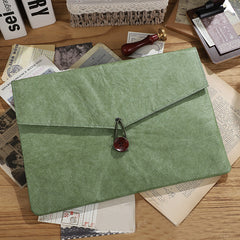 Green textured paper folder with a dark brown button closure on a wooden surface with vintage papers | Shroomi