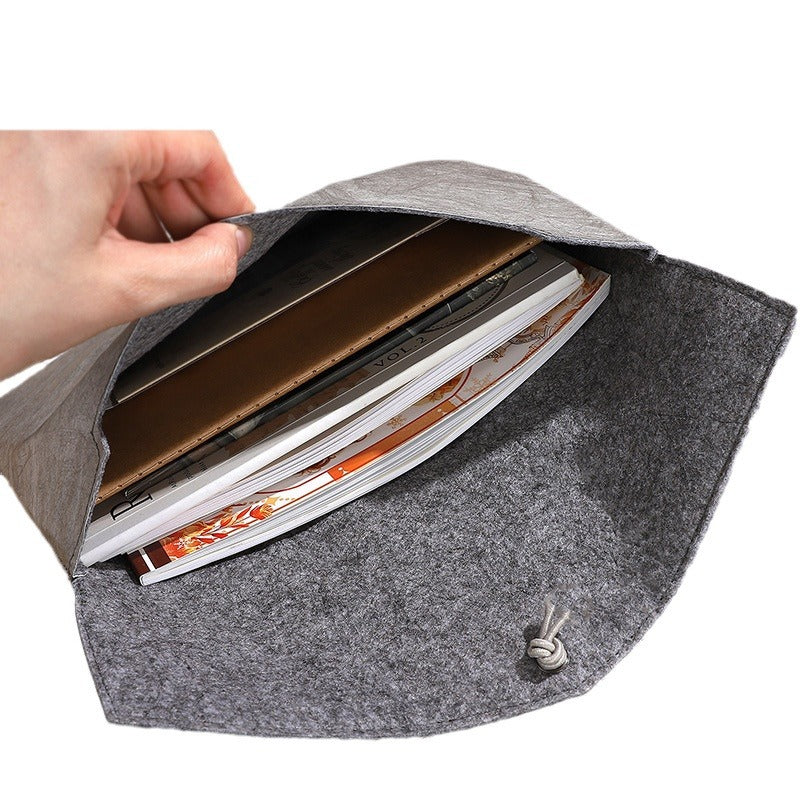 A hand holds open a grey felt envelope clutch filled with notebooks and papers | Shroomi