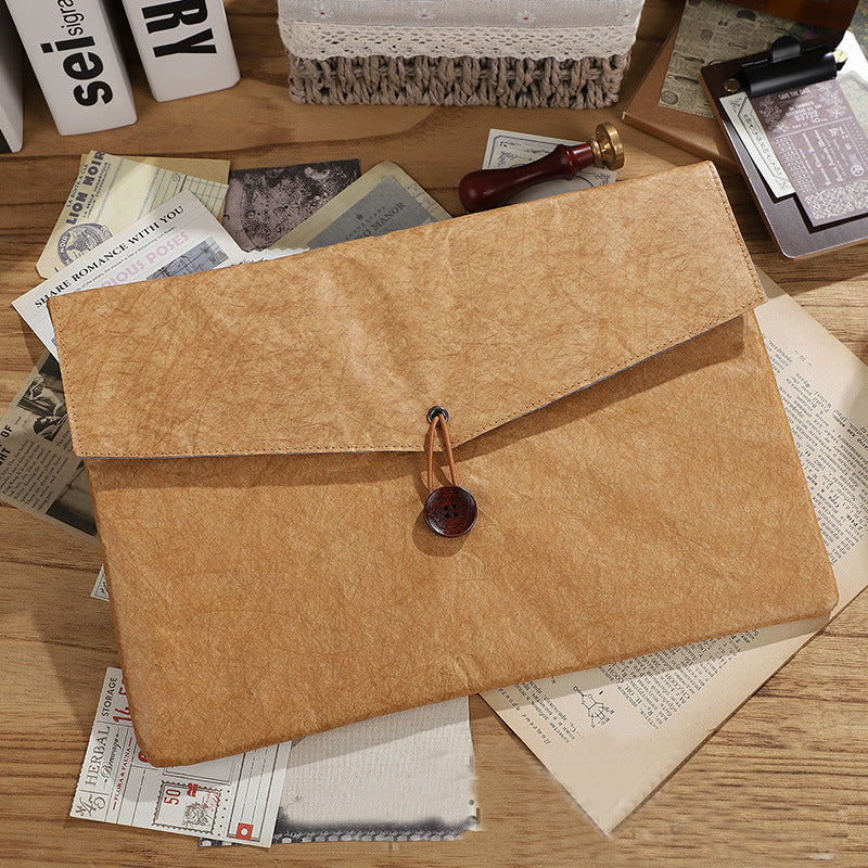 Brown textured paper envelope folder with button closure on desk with vintage papers | Shroomi