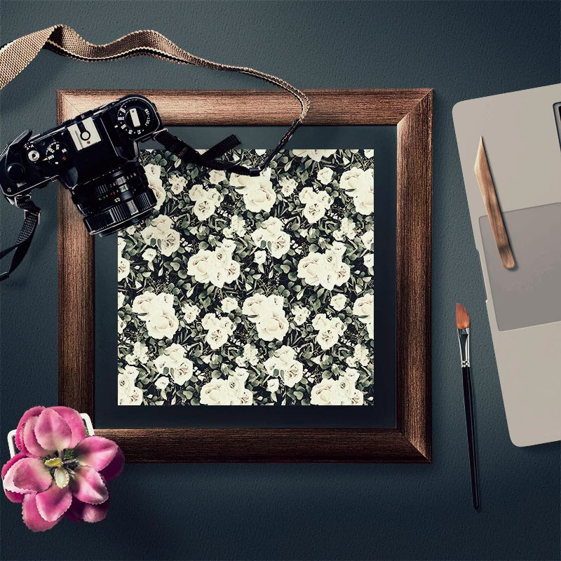 Wood-grained picture frame with a black and white floral pattern inside, next to a camera and art supplies | Shroomi