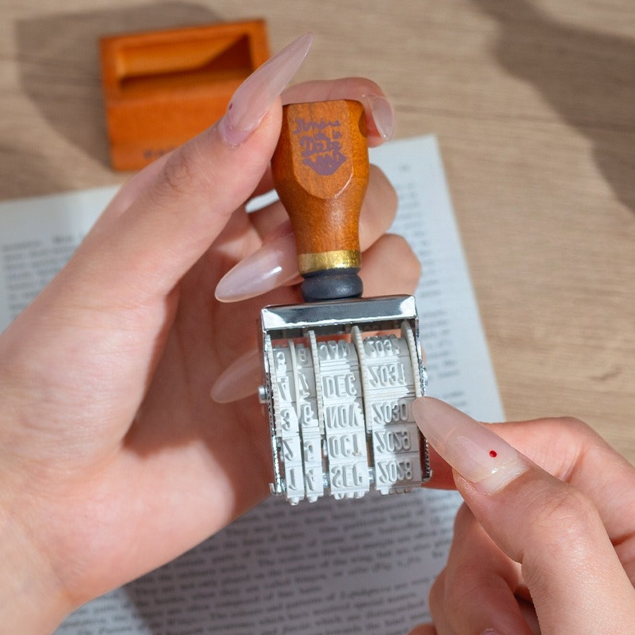 Vintage date roller stamp with wood-style handle, retro postal lettering, metal date wheels, and desk display base