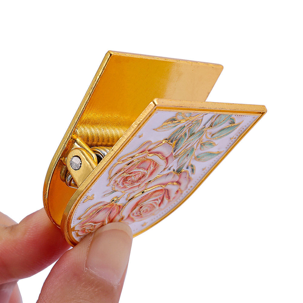 Close-up of the rose-design embossed metal journal clip held open, showing the spring clip mechanism